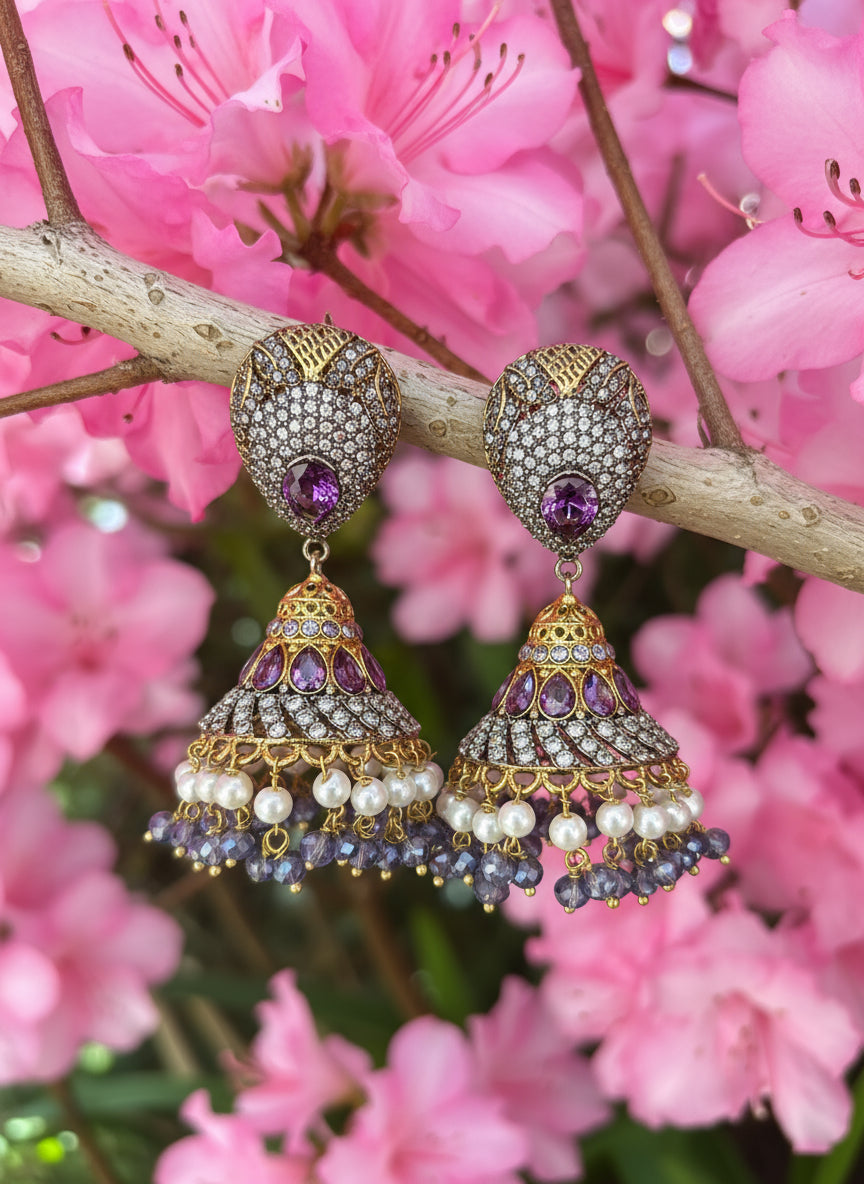 Ornate earrings with purple gemstones and pearl accents on a branch with pink flowers.