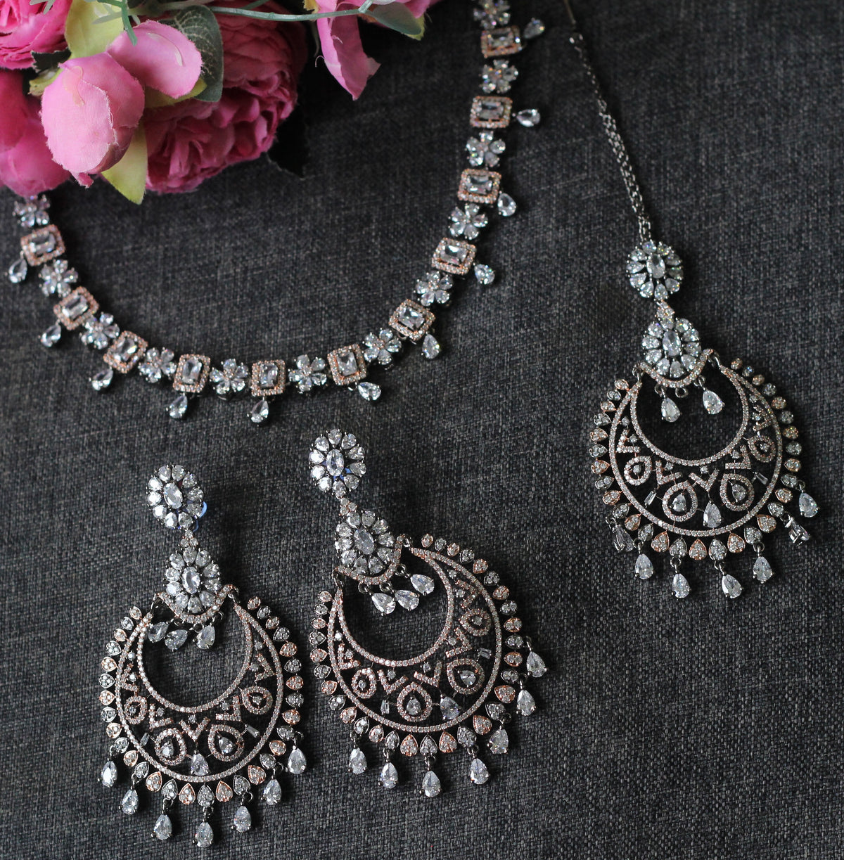 A silver-toned Indian bridal jewelry set featuring a necklace, matching earrings, and a choker, decorated with intricate filigree and clear stones.
